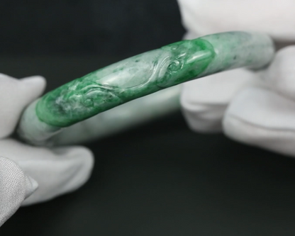 A carved green jade bangle bracelet held by hands wearing white gloves against a dark background.